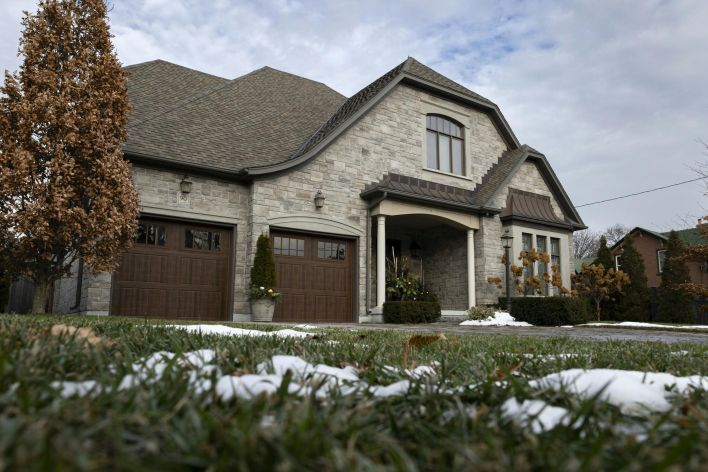 Charming stone house with wooden garage doors and a snow-dusted lawn under a cloudy winter sky.