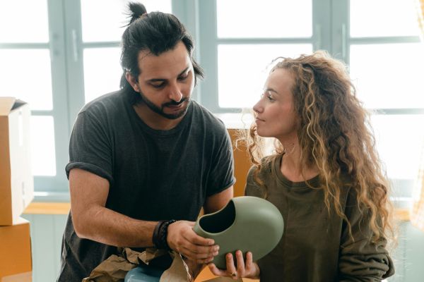 A young couple unpacks a vase in their new apartment, symbolizing a fresh start.